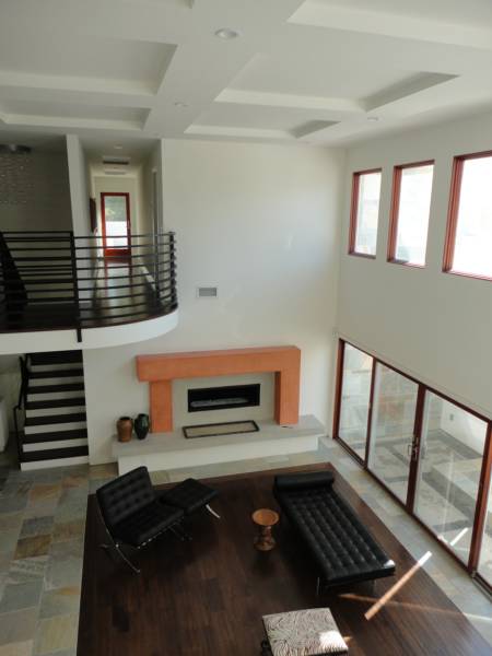 Spacious modern living room with a sleek black sofa, orange fireplace, and large windows offering natural light. Stairs lead to an upper level.