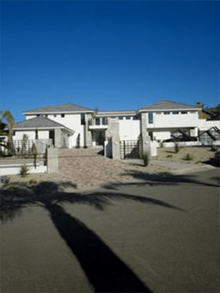 Modern two-story house with a paved driveway and palm trees.
