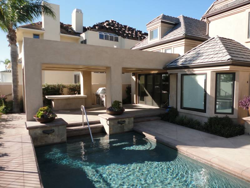 Modern home exterior featuring a swimming pool, outdoor seating area, and a grill.