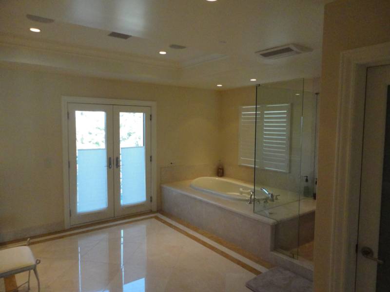 Spacious modern bathroom featuring a freestanding tub, glass shower, and double French doors leading to a bright outdoor view.