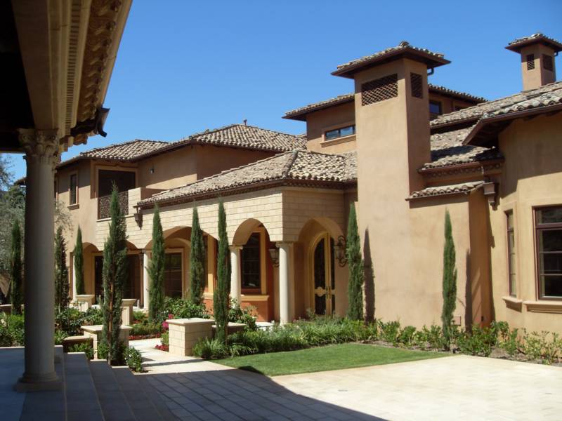 Luxurious Mediterranean-style home with a beautifully landscaped garden, featuring tall cypress trees and arched colonnades